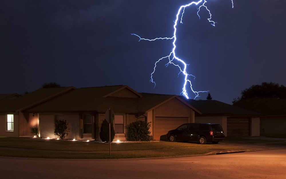 Single‑family home illuminated at night with a lightning strike in the background, symbolizing severe weather and disaster‑response readiness.