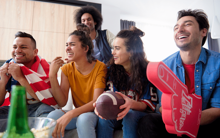 Group of friends watching a football game together on a couch with snacks and fan gear during a gameday gathering in a rental home