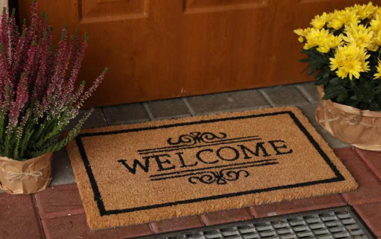 Welcome doormat with potted heather and yellow chrysanthemums by a rental home front door