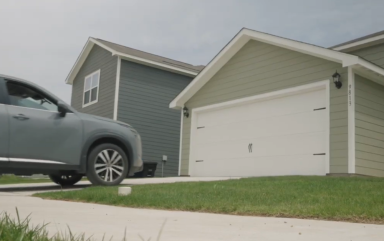 Garage with a closed white garage door and a car parked in the driveway of a rental home.