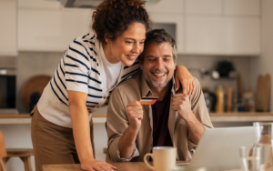 A couple smiling while reviewing finances on a laptop, holding a credit card at home.