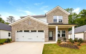 Front exterior of a two-story brick rental home with a white two-car garage, covered front porch, landscaped front yard, and spacious driveway, illustrating a home with ample garage storage potential.