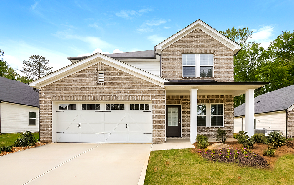 Front exterior of a two-story brick rental home with a white two-car garage, covered front porch, landscaped front yard, and spacious driveway, illustrating a home with ample garage storage potential.