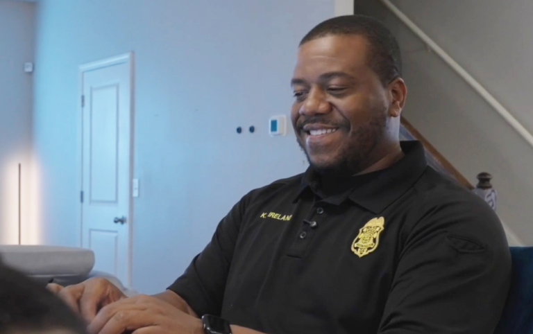 Sargeant Ireland smiles while using a laptop inside a Progress Residential rental home, highlighting how workforce housing provides stable, comfortable homes for officers and their families.