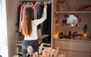 A woman organizes fall clothing in her closet, browsing neutral-colored sweaters and jackets on hangers.