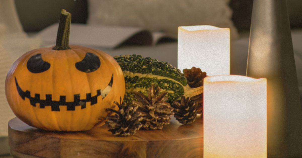 Jack-o’-lantern displayed on a wooden table alongside pinecones, decorative gourds and glowing flameless candles, creating a warm autumn Halloween centerpiece.